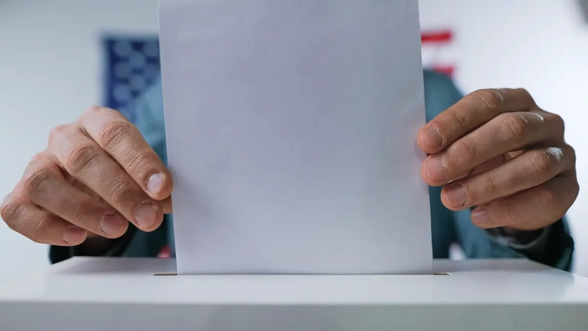 Hands placing a ballot into a ballot box